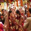 Indian wedding ceremony with brides in traditional attire, adorned with floral garlands, surrounded by guests celebrating amidst vibrant decorations.